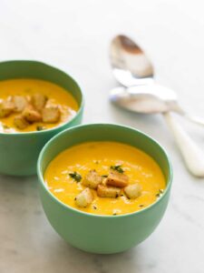 Green bowls of pumpkin beer cheese soup with croutons and spoons.