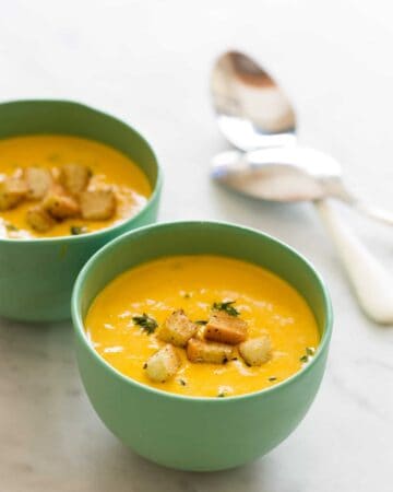 Green bowls of pumpkin beer cheese soup with croutons and spoons.