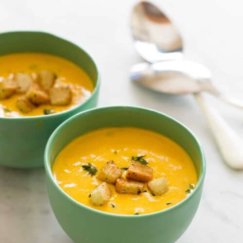 Green bowls of pumpkin beer cheese soup with croutons and spoons.