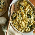 A baking pan of spinach artichoke mac and cheese with a wooden spoon.