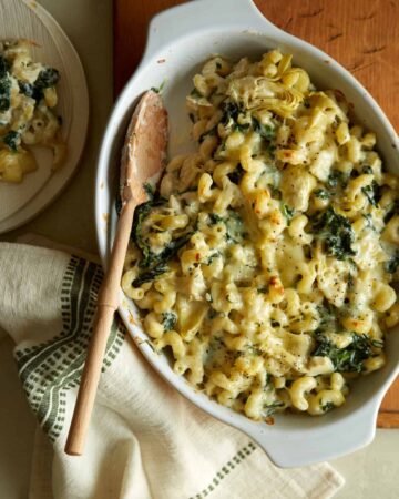 A baking pan of spinach artichoke mac and cheese with a wooden spoon.