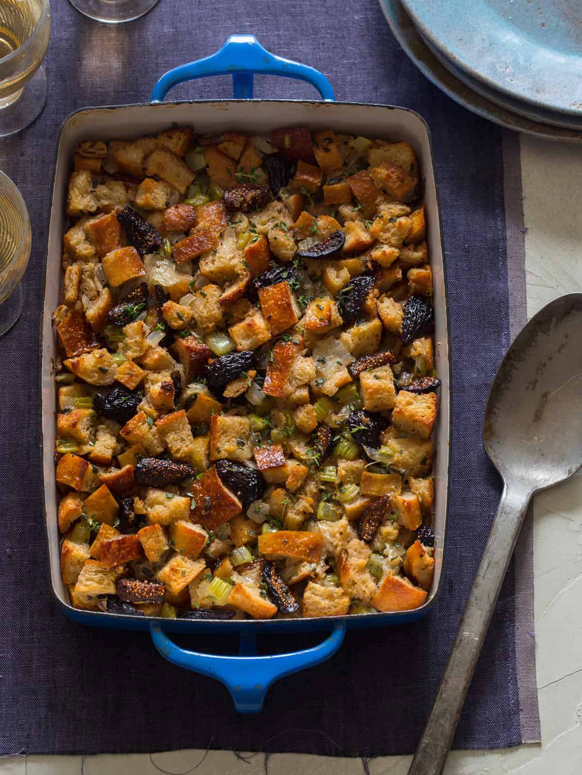 A pan of fig, herb, and sausage stuffing with a serving spoon.