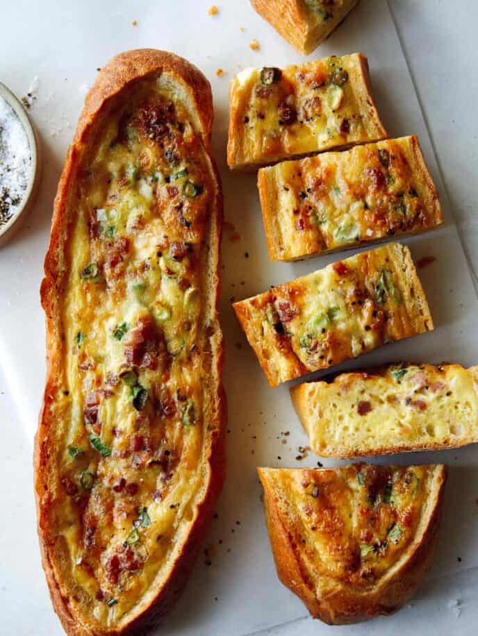 A close up of baked egg boats with a ramekin of pepper and a knife.