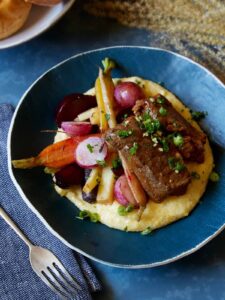A bowl of white wine braised short ribs with vegetables over white cheddar polenta.