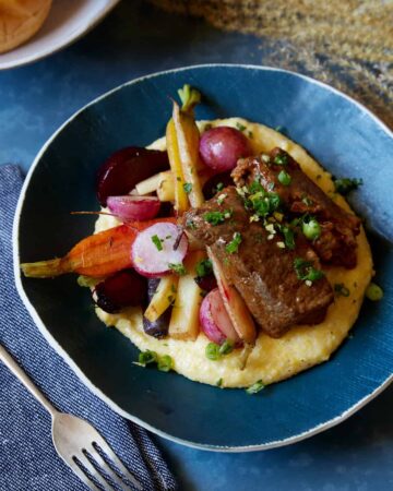 A bowl of white wine braised short ribs with vegetables over white cheddar polenta.