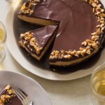 A sliced no bake peanut butter cheesecake with dark chocolate ganache with plates served.