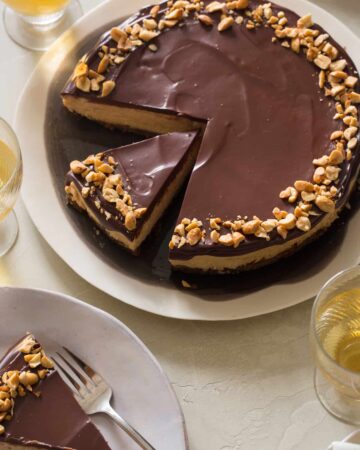 A sliced no bake peanut butter cheesecake with dark chocolate ganache with plates served.