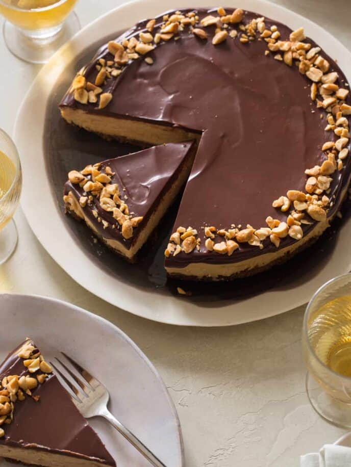 A sliced no bake peanut butter cheesecake with dark chocolate ganache with plates served.