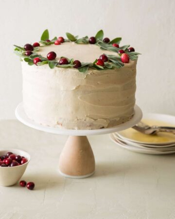 Apple cranberry cake with brown sugar buttercream decorated with fresh cranberries with plates and forks.
