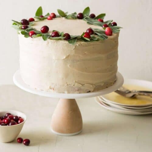 Apple cranberry cake with brown sugar buttercream decorated with fresh cranberries with plates and forks.