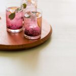 Glasses of blackberry and meyer lemon gin and tonics on a wooden board.