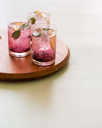 Glasses of blackberry and meyer lemon gin and tonics on a wooden board.
