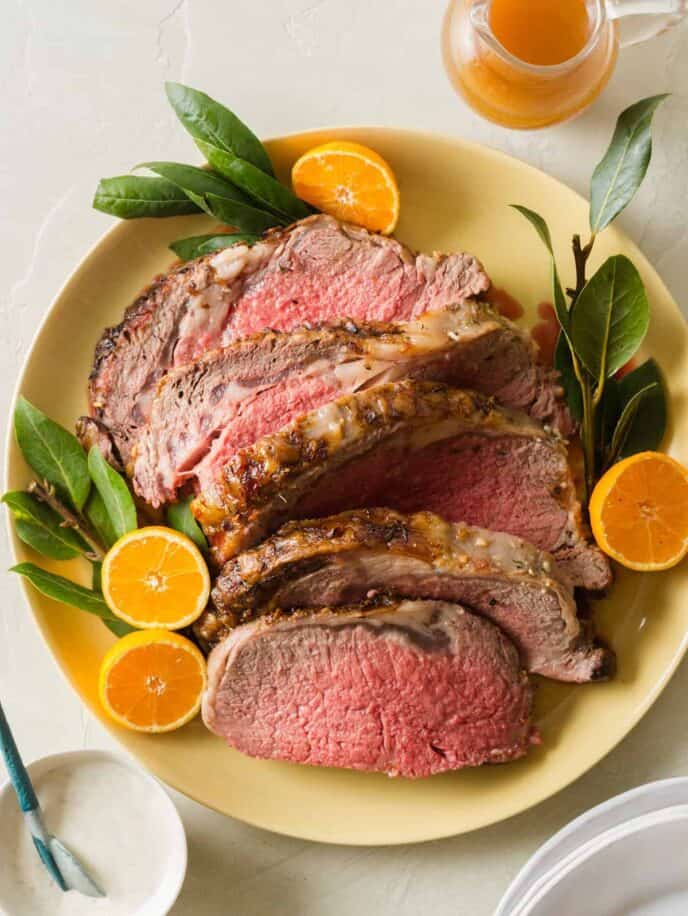 A plate of sliced standing rib roast garnished with orange halves.