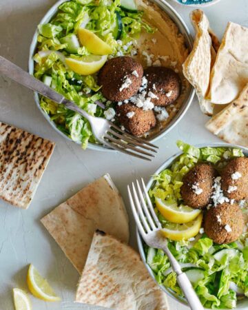 Falafel salad hummus bowls with forks and grilled pita bread.