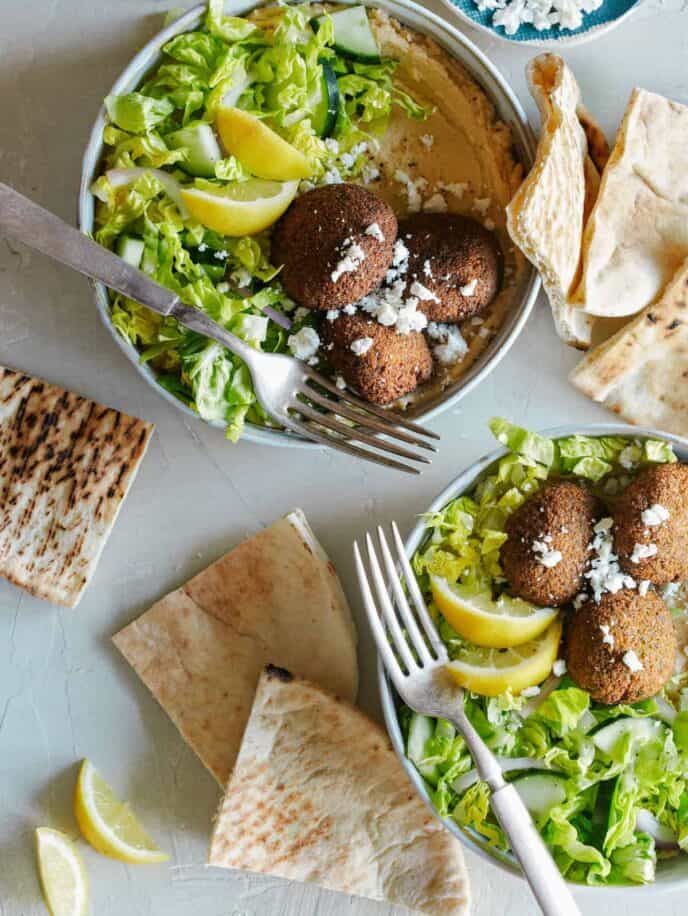 Falafel salad hummus bowls with forks and grilled pita bread.