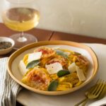 A plate of linguine with butternut squash vegan cream sauce at a set table with wine.