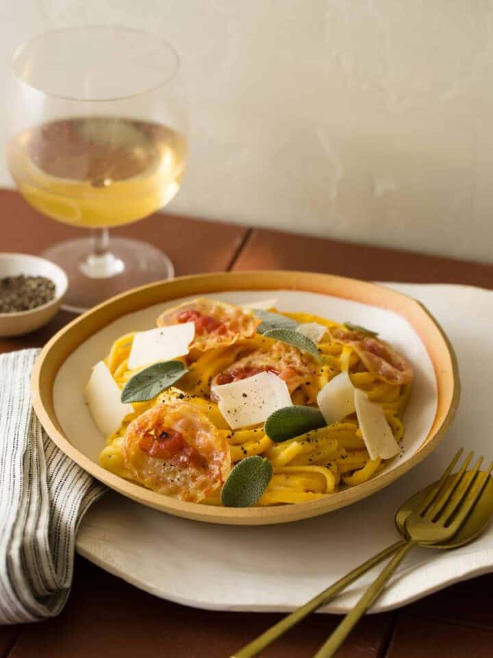 A plate of linguine with butternut squash vegan cream sauce at a set table with wine.