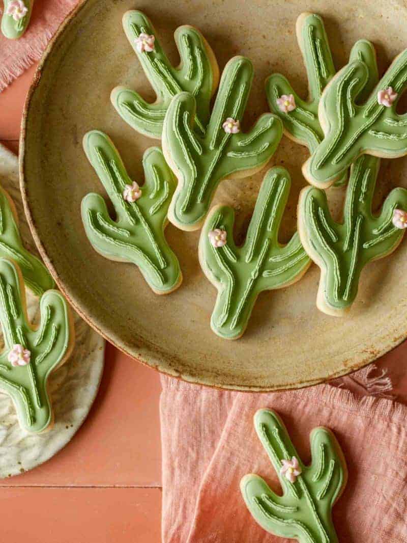 A close up of cactus cookies on a platter, a plate, and a napkin.