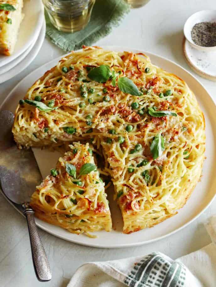 A sliced carbonara pasta pie with a silver pie server and small plates.