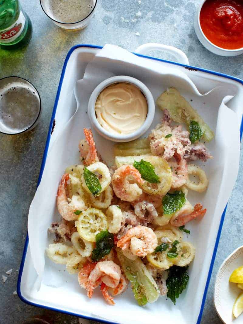 A pan of light and crispy fritto misto with a ramekin of aoli and drinks.