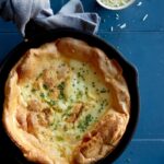 Herb and cheese dutch baby in a skillet with a towel around the handle.