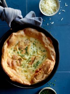 Herb and cheese dutch baby in a skillet with a towel around the handle.