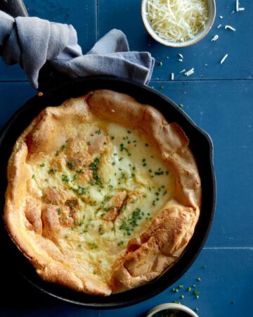 Herb and cheese dutch baby in a skillet with a towel around the handle.
