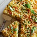 A close up of a sliced carbonara pasta pie with a silver pie server.