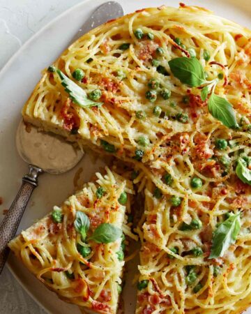 A close up of a sliced carbonara pasta pie with a silver pie server.