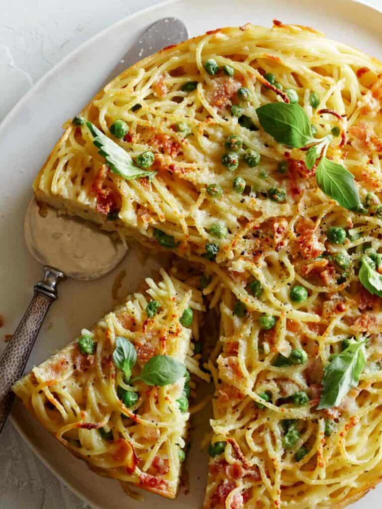 A close up of a sliced carbonara pasta pie with a silver pie server.