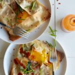 Plates of ham, spinach, and swiss stuffed breakfast crepes with forks.