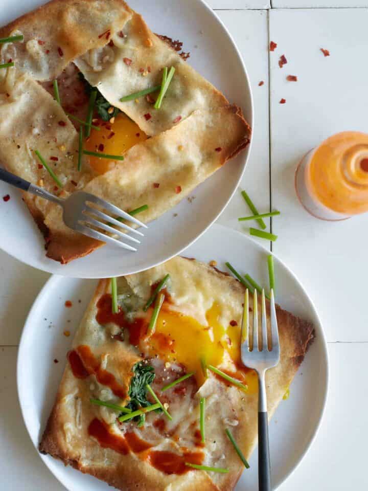 Plates of ham, spinach, and swiss stuffed breakfast crepes with forks.