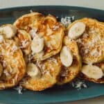 A close up of a plate of coconut banana pancakes with fresh bananas and shredded coconut.