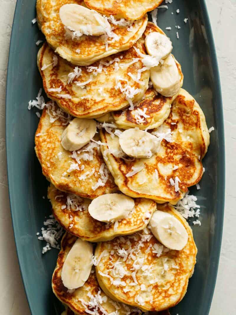 A close up of coconut banana pancakes with fresh bananas and coconut flakes.