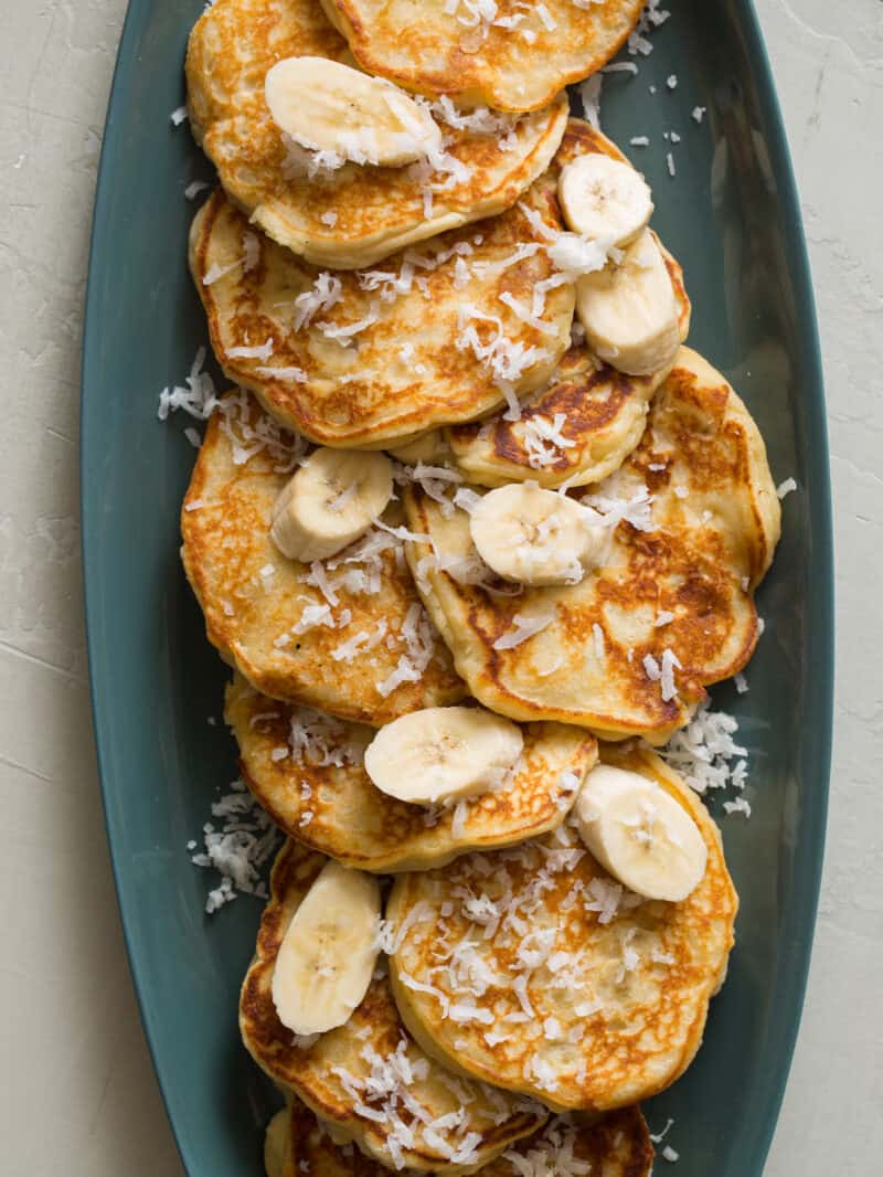 A platter of coconut banana pancaked with fresh bananas and coconut flakes.