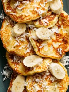 A close up of coconut banana pancakes with fresh bananas and coconut flakes.