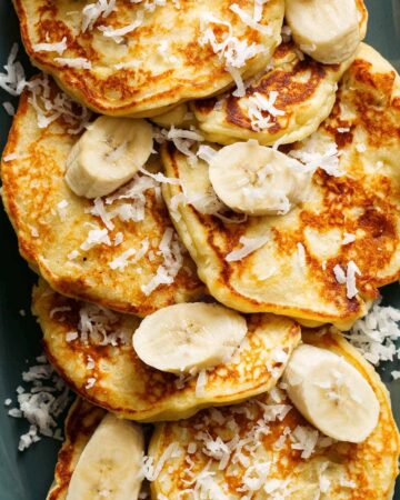 A close up of coconut banana pancakes with fresh bananas and coconut flakes.