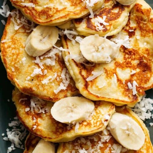 A close up of coconut banana pancakes with fresh bananas and coconut flakes.