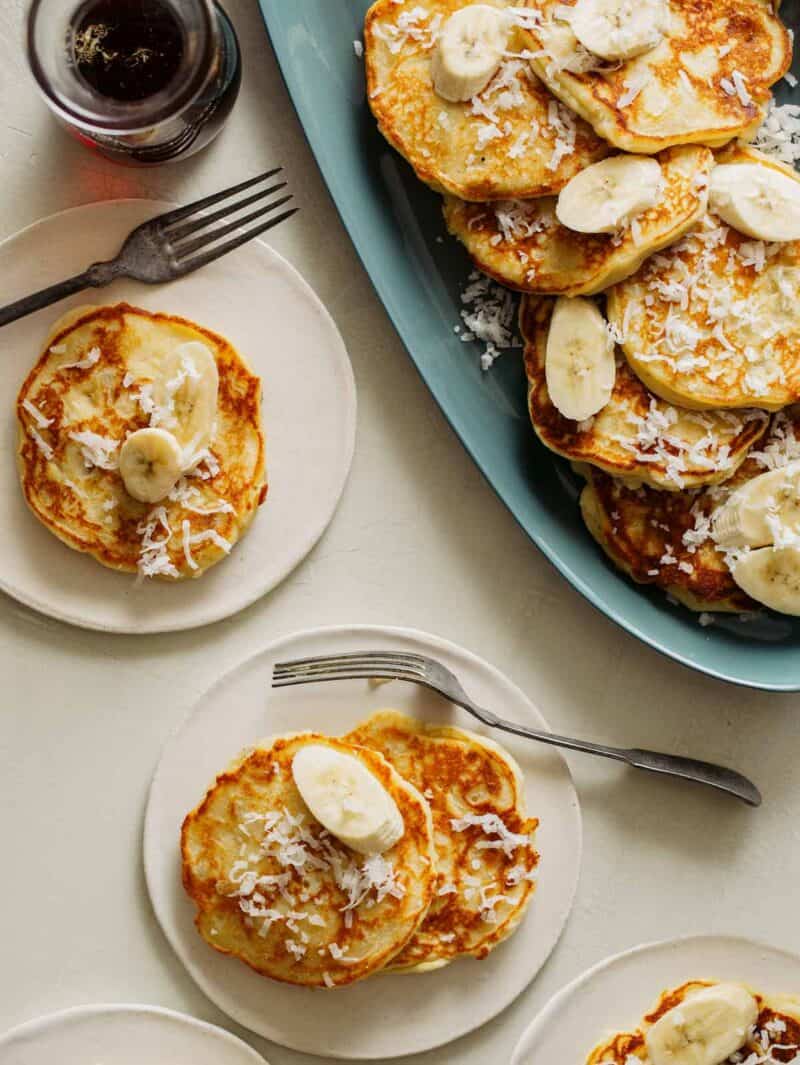 A platter of coconut banana pancakes with servings on small plates and forks.