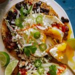 A plate of huevos rancheros with black beans and chipotle salsa with a fork.