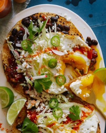 A plate of huevos rancheros with black beans and chipotle salsa with a fork.