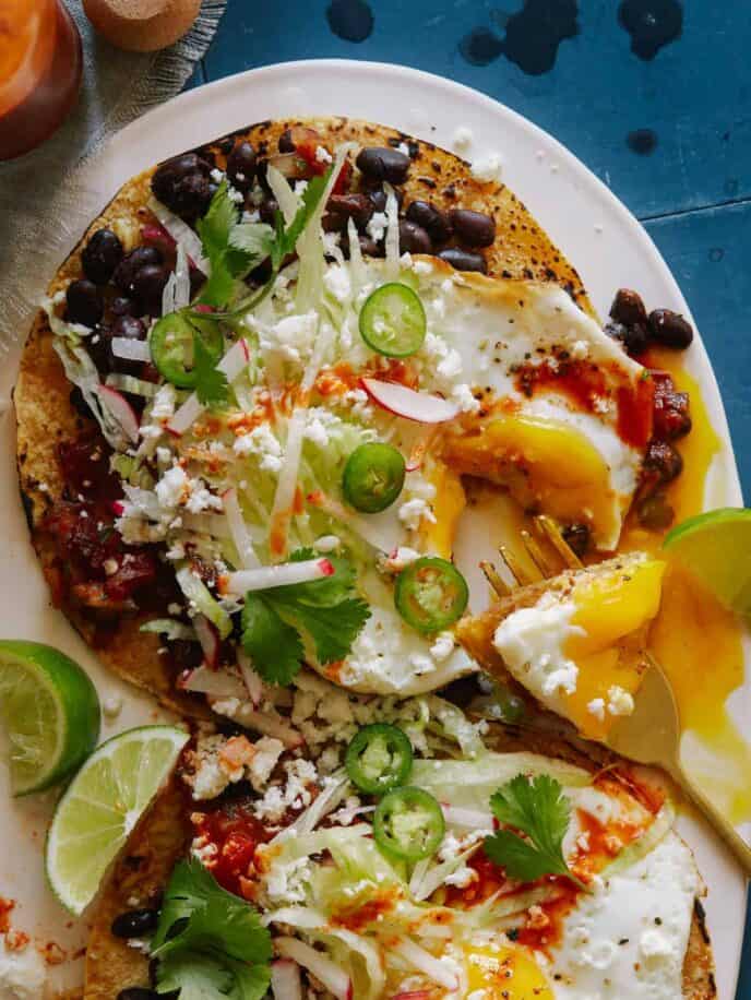 A plate of huevos rancheros with black beans and chipotle salsa with a fork.