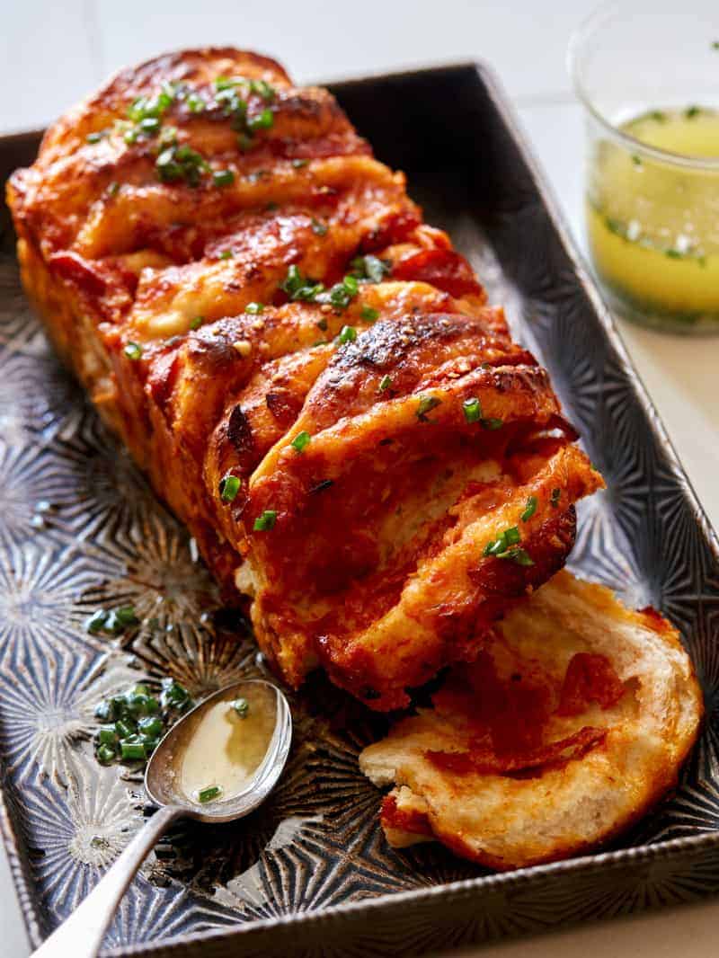 A close up of pull apart pizza bread with garlic herb butter and a spoon.
