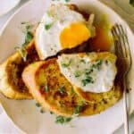 A plate of savory herb french toast with a broken egg yolk and a fork.