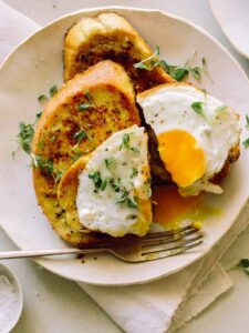 A plate of savory herb french toast with a broken egg yolk and a fork.