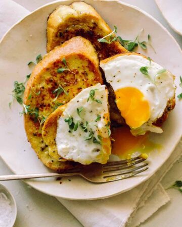 A plate of savory herb french toast with a broken egg yolk and a fork.