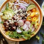 Carne Asada Burrito bowl with a lot of toppings, and avocado on the side, with another bowl peeking in.