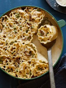 Chicken alfredo lasagne roll ups in a pan, serving with a spoon.