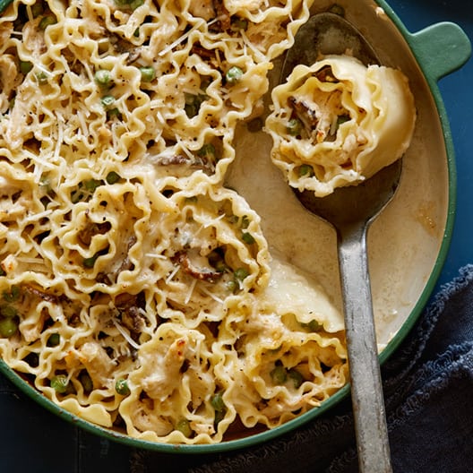 Chicken alfredo lasagne roll ups in a pan, serving with a spoon.