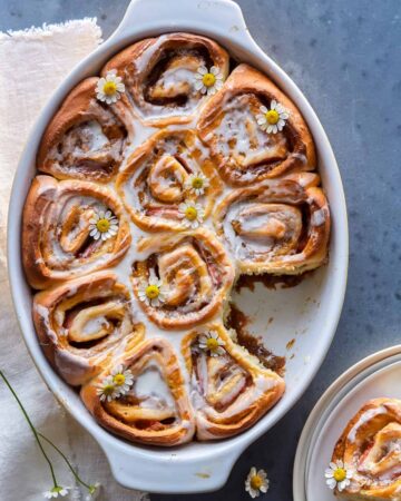 An baking dish of strawberry cinnamon rolls with chamomile and vanilla glaze with one removed.